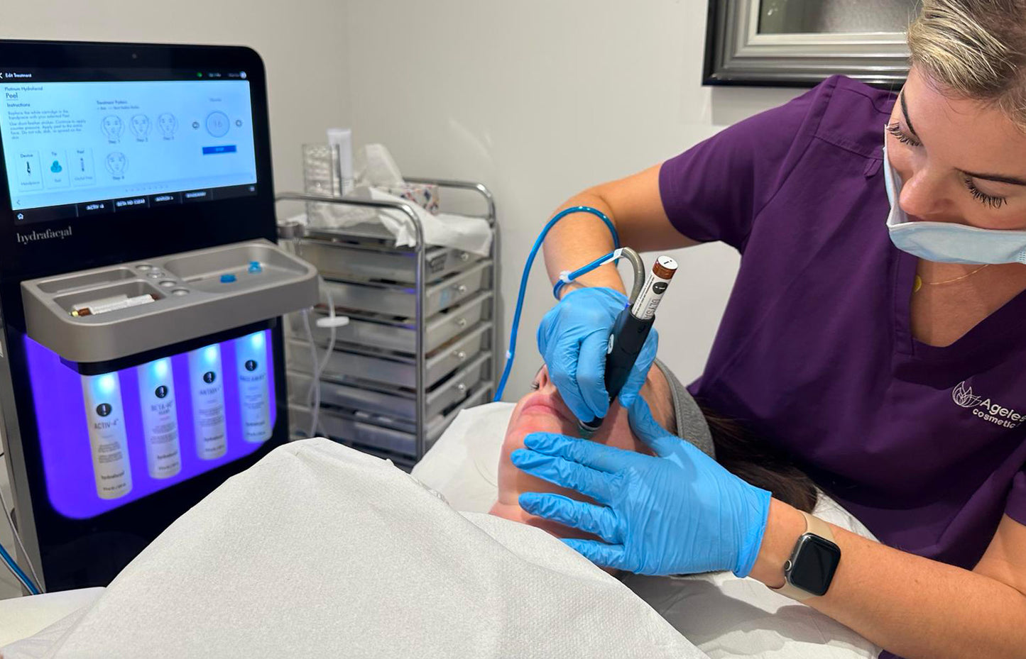 Person receiving a medical procedure with a technician applying equipment to their head.