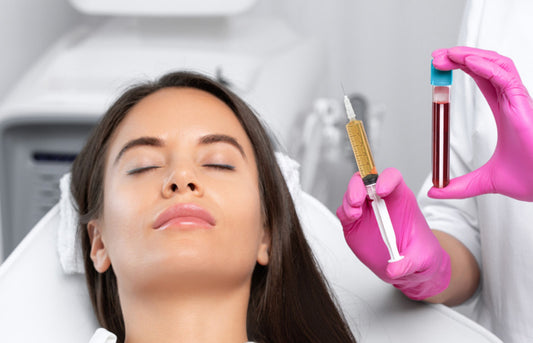 Woman receiving a blood test with a healthcare professional holding a syringe and blood sample tube.