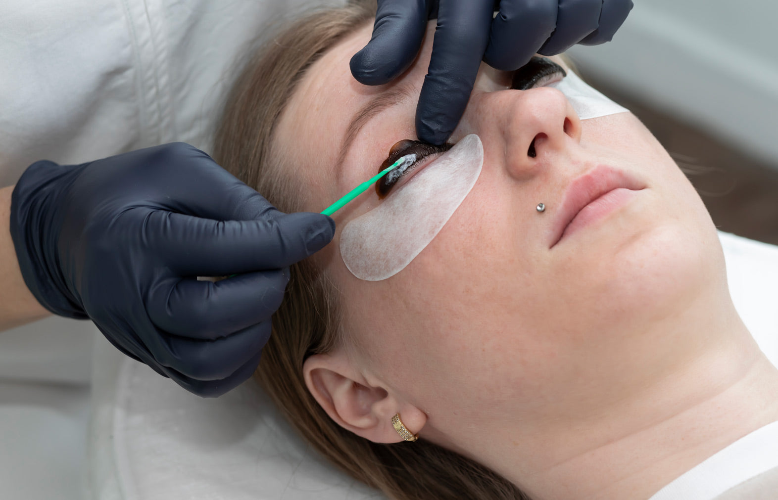 Person receiving an eye examination with a green tool, wearing gloves.