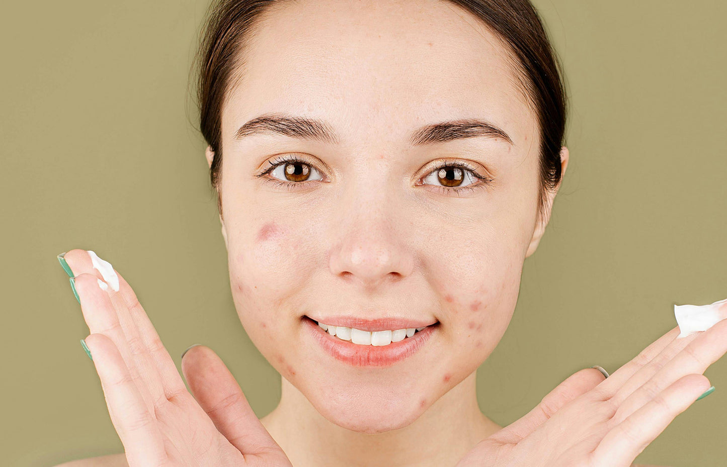 Woman applying cream to her face with a green background