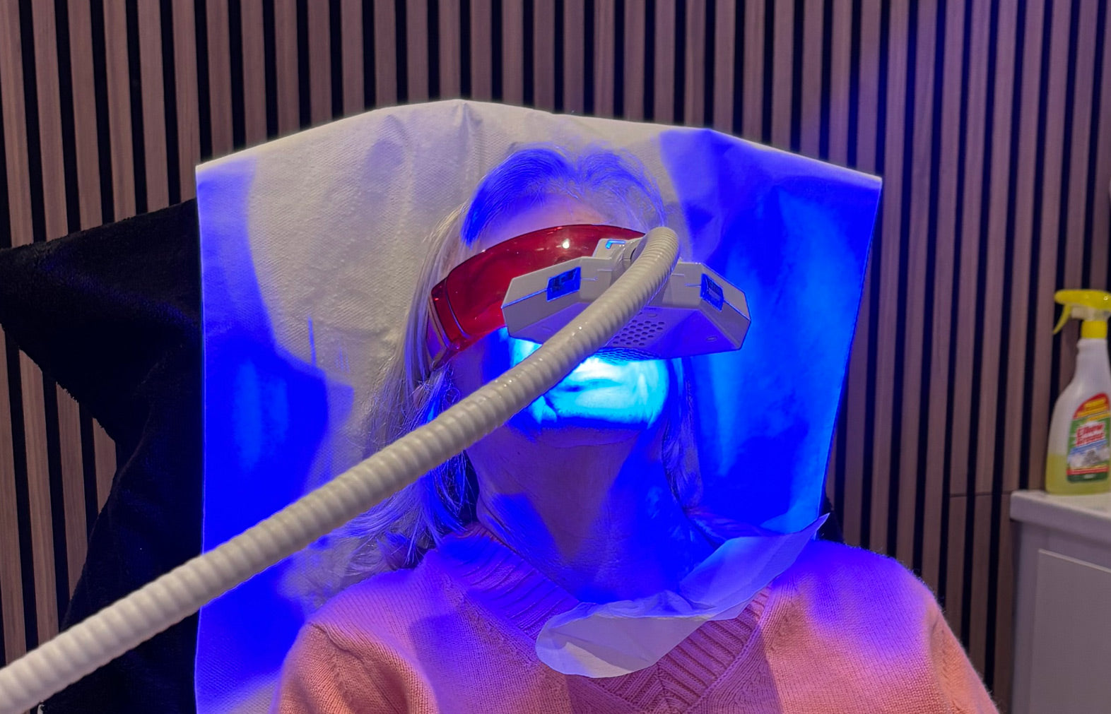 Person wearing a LED face mask with blue light in a room.